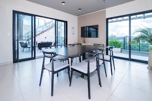 Een moderne eetkamer met een grote tafel en stoelen, grote ramen en een trap naar een buitenruimte.