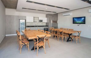 Eine moderne Küche mit integrierten Geräten, ein Essbereich mit Holztischen und -stühlen sowie ein flachbildfernseher an der Wand.