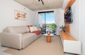 Ein modernes Wohnzimmer mit einer Couch, einem Couchtisch, einem an der Wand befestigten Fernseher und einem Balkon mit Sitzgelegenheiten.