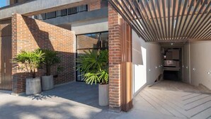 A modern building with a brick facade, large windows, and a covered entrance area with potted plants. - Modern 1BR Near Shopping del Sol | Pool & Gym (Asunción)