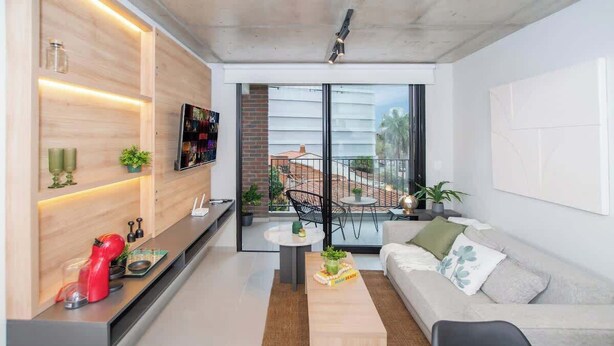 A modern living room with a sofa, coffee table, and a TV on a wooden wall. - Modern 1BR Near Shopping del Sol | Pool & Gym (Asunción)