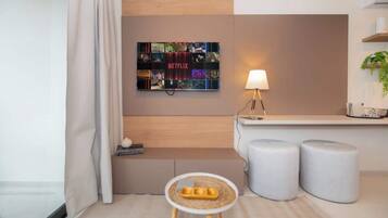 Une chambre d’hôtel moderne avec une décoration murale inspirée de Netflix, une petite table ronde avec un plateau, et deux poufs.