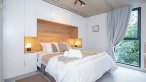 Una camera da letto con un letto, lampade sui comodini, una finestra con tende e vista su del verde all'esterno.