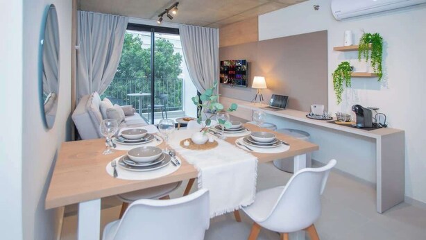 Un'area pranzo moderna con un tavolo in legno apparecchiato per quattro persone, sedie bianche e vista sul verde.