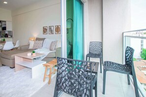 Ein modernes Wohnzimmer mit einer Couch, einem Couchtisch und Sesseln, ein Balkon mit Blick und ein Essbereich mit Tisch und Stühlen.