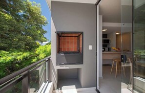 Ein Balkon mit Blick auf Bäume, eine Küchenzeile mit Mikrowelle und eine Schiebetür.