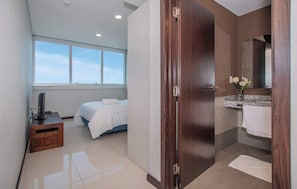 A modern hotel room with a large window, a bed, a vanity with a mirror, and a wooden door. - Bright 3BR Escape, City Views, Pool & Gym (Asunción)