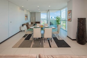 A modern dining area with a glass table, white chairs, and a city view. - Bright 3BR Escape, City Views, Pool & Gym (Asunción)