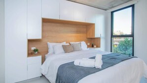 Una camera da letto moderna con un letto grande, una testiera in legno integrata, comodini e un'ampia finestra.
