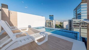 Una piscina sul tetto con lettini, vista chiara sullo skyline cittadino e moderni edifici sullo sfondo.