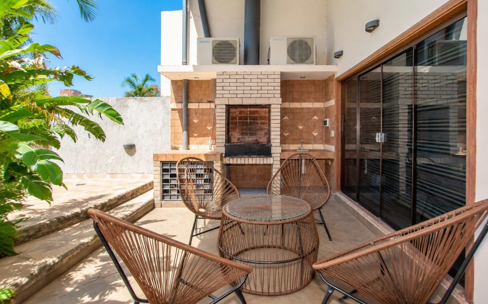 An outdoor patio with a brick fireplace, wicker chairs, and a glass table.