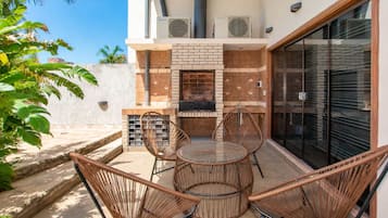 An outdoor patio with a brick fireplace, wicker chairs, and a glass table.