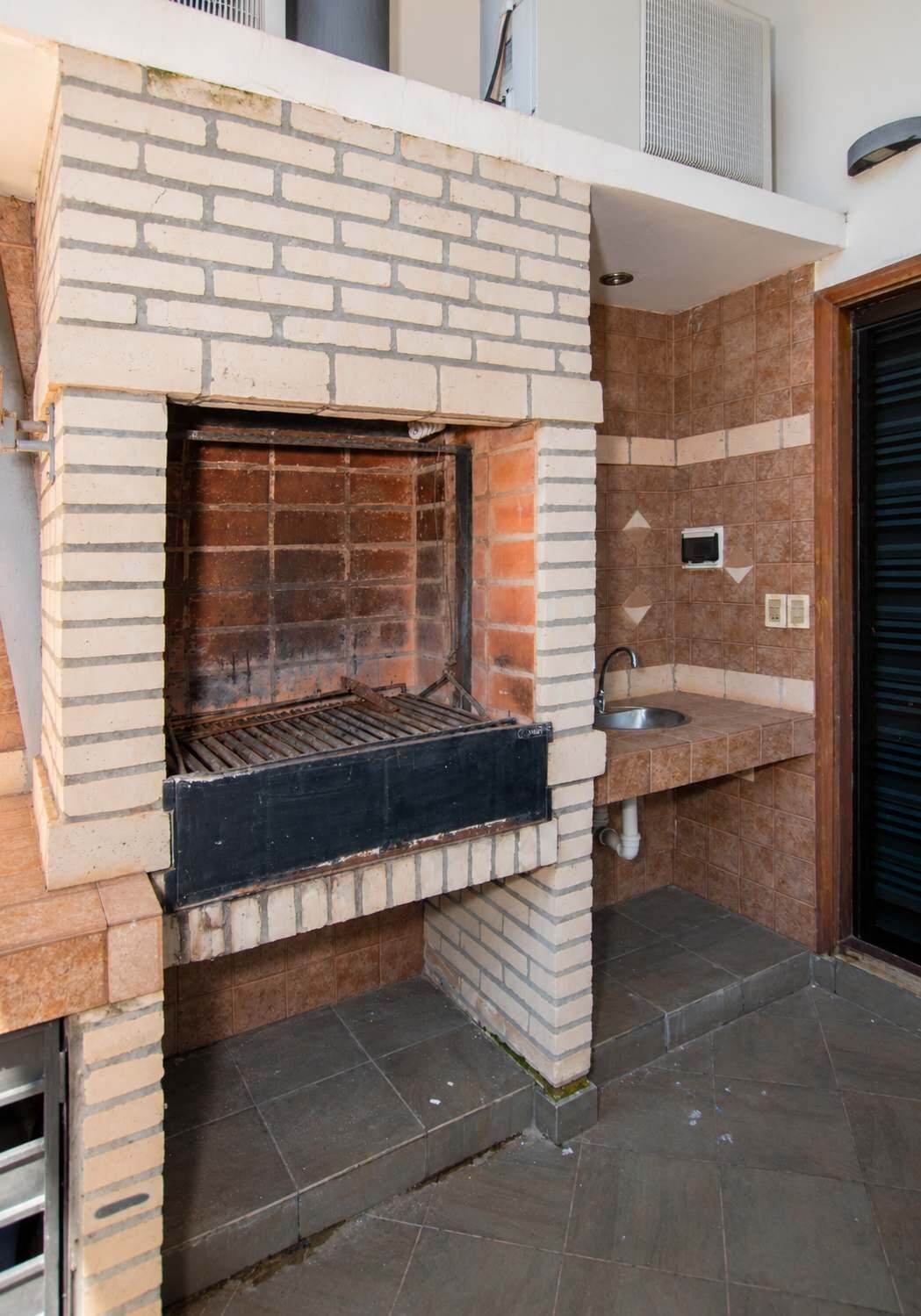 A brick-built outdoor kitchen with a grill, a sink, and a tiled backsplash.