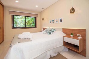Un dormitorio moderno con una cama grande, una mesita de noche con una planta, una ventana con vistas a árboles y un aplique de pared.