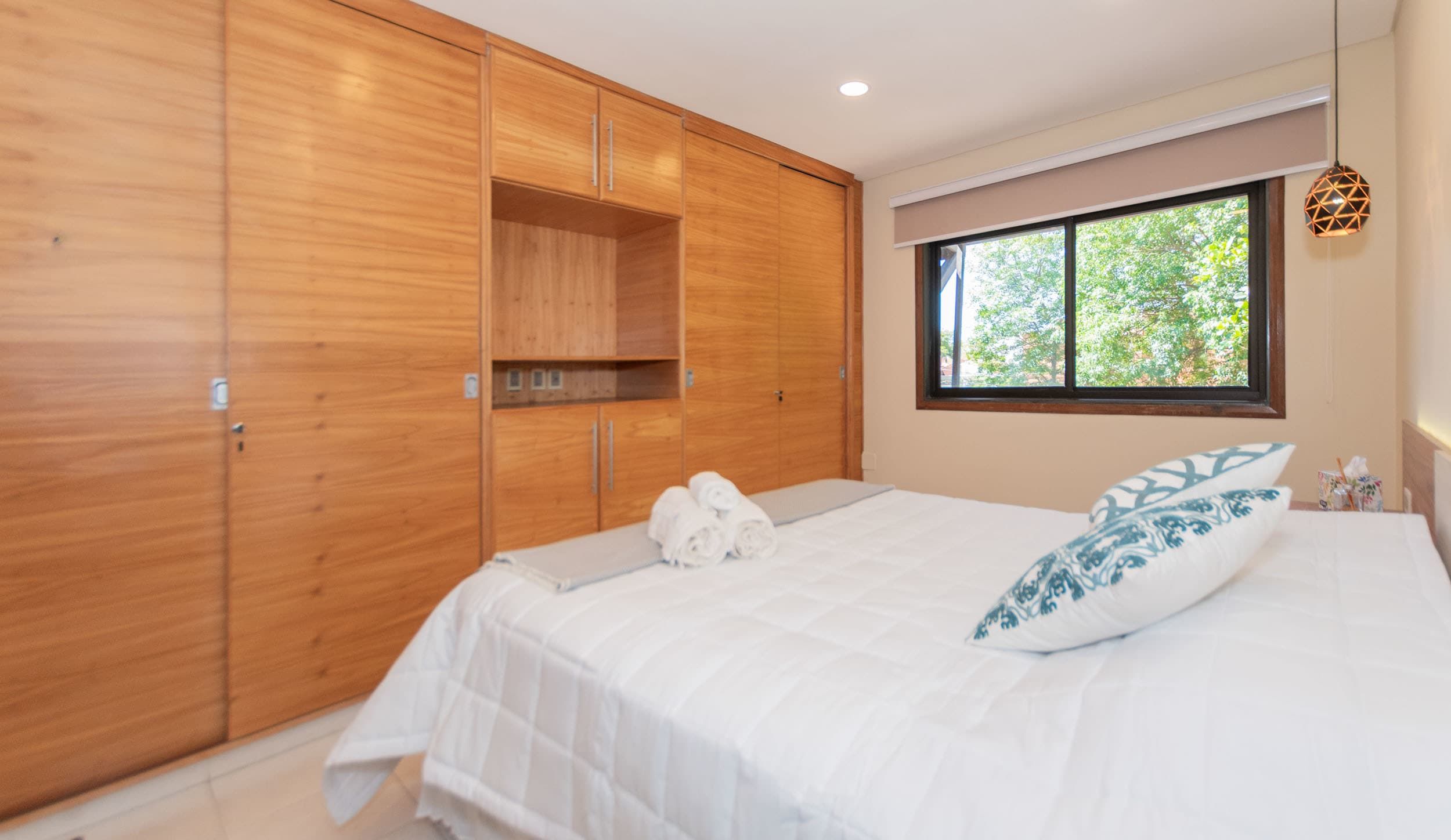 A bedroom with a bed, a window, and wooden wardrobe.