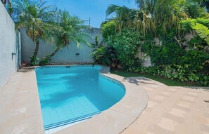 A swimming pool with a curved edge, surrounded by a concrete deck and lush greenery. - Spacious Mburucuyá Duplex | Pool, BBQ & Jacuzzi (Asunción)