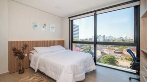 Une chambre moderne avec une grande fenêtre, un lit, un bureau et une vue sur la ville.