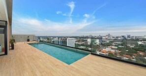 A rooftop pool with a city view, wooden deck, and a glass railing. - Modern Studio near Malls | Gym & Rooftop Pool (Asunción)