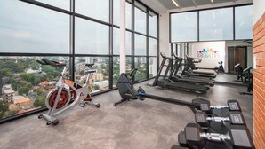 Une salle de sport équipée de tapis de course, de vélos d’appartement et d’haltères, de grandes fenêtres offrant une vue sur la ville et d’une enseigne indiquant « Elite Fitness ».