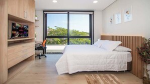 A bedroom with a bed, a desk, a TV, and a large window. - Chic Studio Near Malls with Pool and Gym (Asunción)