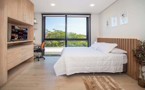 A bedroom with a bed, a desk, a TV, and a large window. - Chic Studio | Malls, Pool, Gym & Rooftop View (Asunción)