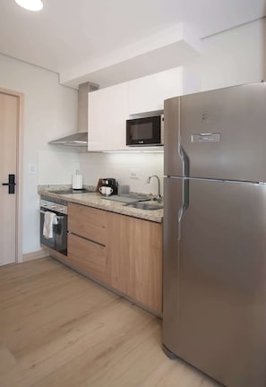 A modern kitchen with stainless steel appliances, wooden cabinets, and a microwave. - Chic Studio | Malls, Pool, Gym & Rooftop View (Asunción)