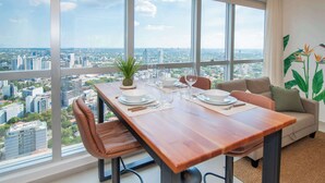 A dining area with a wooden table, chairs, and a city view through large windows. - Modern One BR in Petra Tower, Skyline Views & Pool (Asunción)