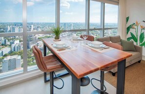 Un comedor con mesa de madera, sillas y vistas a la ciudad a través de amplios ventanales.