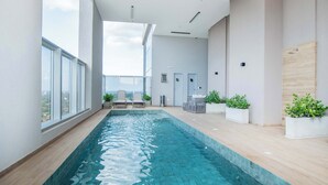 Una piscina interior moderna amb aigua blava cristal·lina, envoltada de parets blanques i grans finestres que ofereixen una vista a la ciutat.