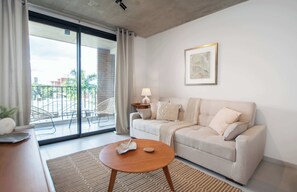Un salon avec un canapé, une table basse, une lampe et une vue sur l’extérieur, accessible par une porte-fenêtre coulissante.