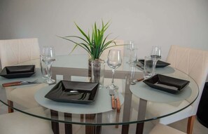 A dining table with a glass top, surrounded by chairs, with a plant in a vase, and wine glasses and cutlery on the table.