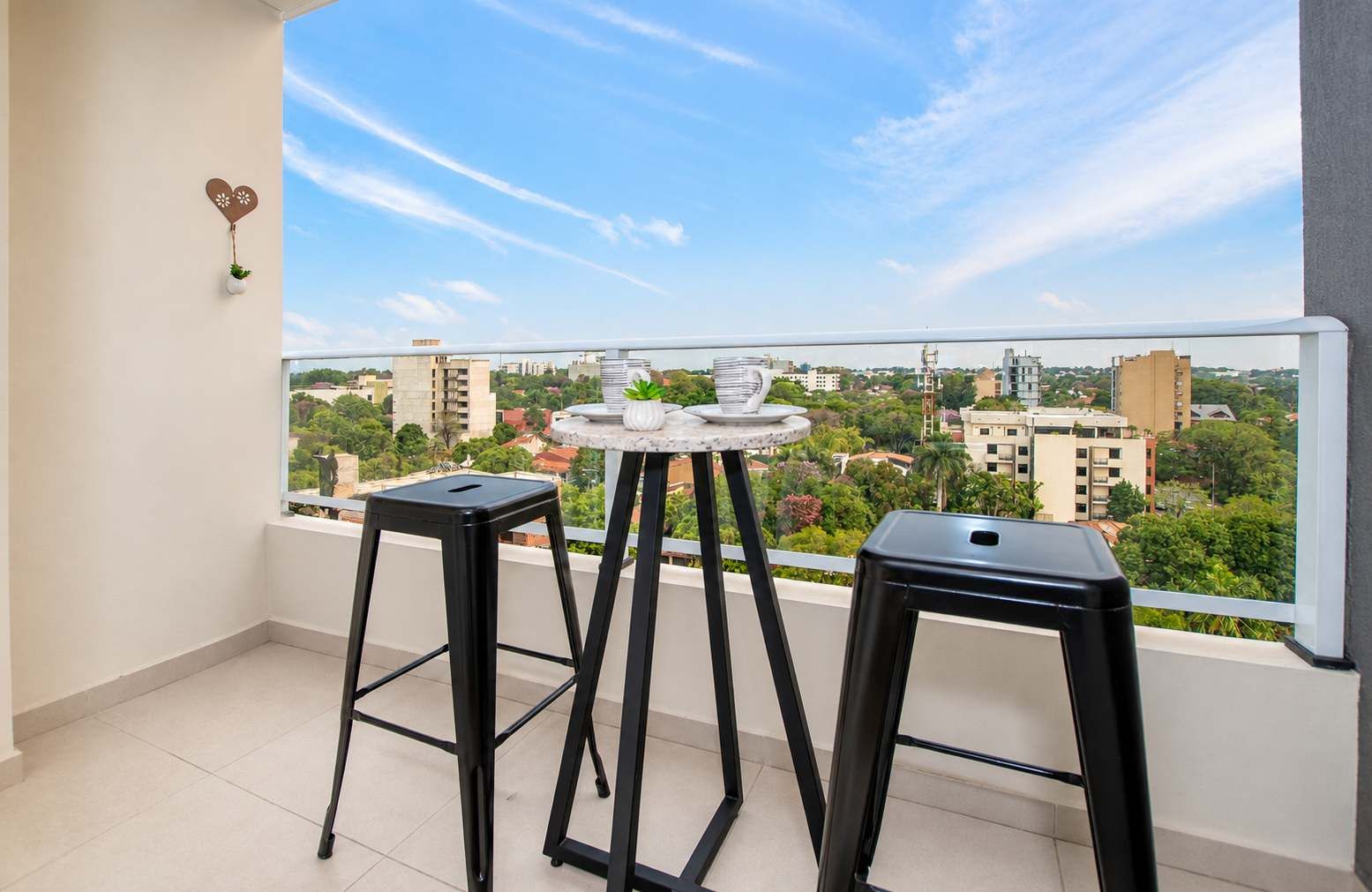 A balcony with two black stools and a small round table with a white vase and a plant.