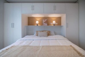 Une chambre à coucher comprenant un lit, une table de chevet, une étagère fixée au mur avec deux lampes et une tête de lit.
