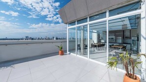 Een modern gebouw met grote glasramen, een terras op het dak en uitzicht op de stadshemel.