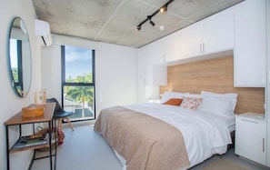 A modern bedroom with a large bed, a desk, and a view of greenery outside. - Apartment Near Malls with Pool, Gym, Cinema&WiFi (Asunción)