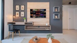 Un saló modern amb televisió de pantalla plana penjada a la paret, una taula de consola de fusta, una cadira negra i una petita taula auxiliar amb una planta.