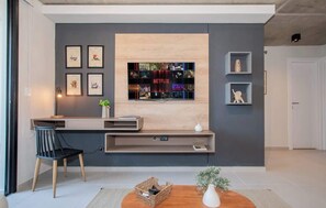 A modern living room with a flat-screen TV mounted on a wall, a wooden console table, a black chair, and a small side table with a plant. - Apartment Near Malls with Pool, Gym, Cinema&WiFi (Asunción)