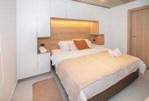 Un dormitorio moderno con una cama grande, paredes blancas, cabecera de madera y mesita de noche empotrada.