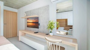 Een moderne kamer met een houten bureau, een wandgemonteerde televisie, een bed en een spiegel die de kamer weerspiegelt.