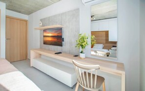 Quarto moderno com escrivaninha de madeira, televisão montada na parede, cama e espelho refletindo o ambiente.