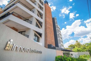 Un edificio de varios pisos con balcones, una chimenea de ladrillo destacada y un letrero que dice 'Innoval Los Mercedes'.