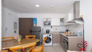 Cozinha compacta com mesa de jantar, cadeiras, máquina de lavar, micro-ondas e fogão.