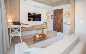 A modern living room with a sofa, a small table, a white chair, a wooden desk, and a wall-mounted TV. - Business Gem w/ Pool & Gym | Near Malls | 400Mbps (Asunción)