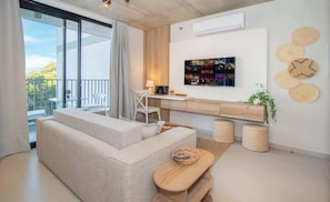 Uma sala de estar moderna com sofá, escrivaninha, poltrona, TV na parede e varanda com vista.