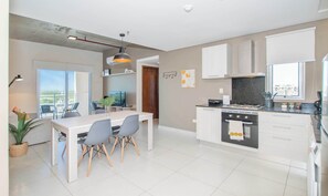 Una cocina moderna con una isla central, armarios blancos y un comedor con mesa y sillas.