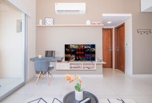 Una sala de estar moderna con un televisor de pantalla plana, un escritorio, una silla y una planta en maceta.