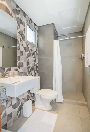 Un baño con ducha, inodoro, lavamanos y una pared con diseño geométrico.