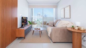 Una sala moderna con sofá, mesa de centro, televisor y un balcón con vistas.