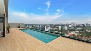 Ein Pool auf dem Dach mit Blick auf die Stadt, Holzboden und eine Glasbrüstung.