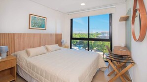 Ein Hotelzimmer mit einem großen Bett, einem Schreibtisch, einem Sessel, einem Fenster mit Aussicht und einem Bild an der Wand.